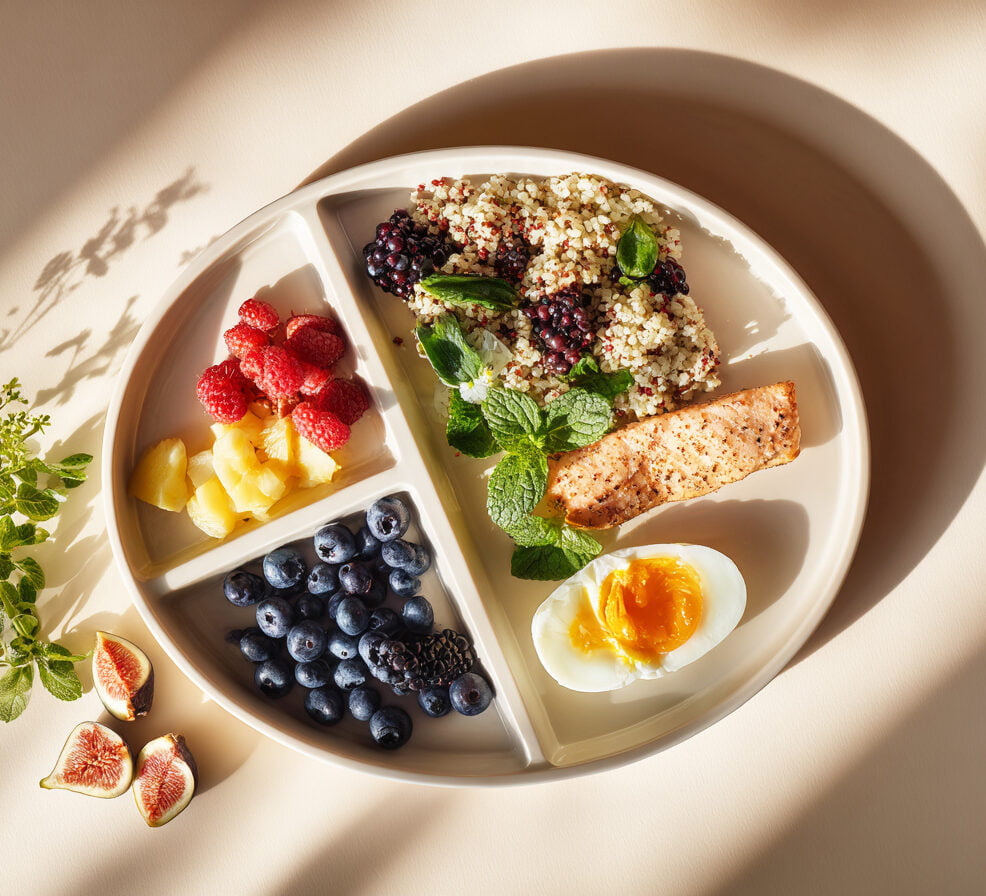 Foto eines Partitionstellers mit Beeren, Quinoa und Lachs und Ei, KI-generiert