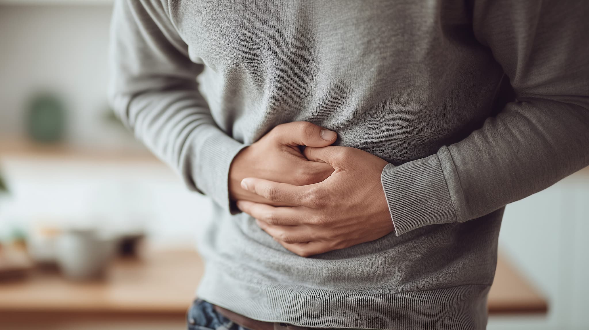 Mann in einem grauen Pullover, der sich den Bauch hält, möglicherweise wegen Bauchschmerzen – KI-generiert